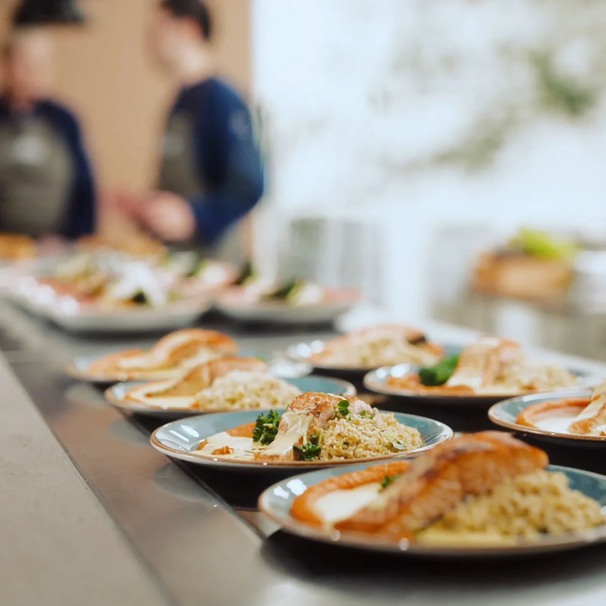 Tallerkner på rad med to Coor - kokker diffust i bakgrunnen